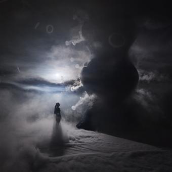 An atmospheric photo which shows a figure standing looking up at the infinity blue sculpture and the vapour surrounding the floor and sculpture